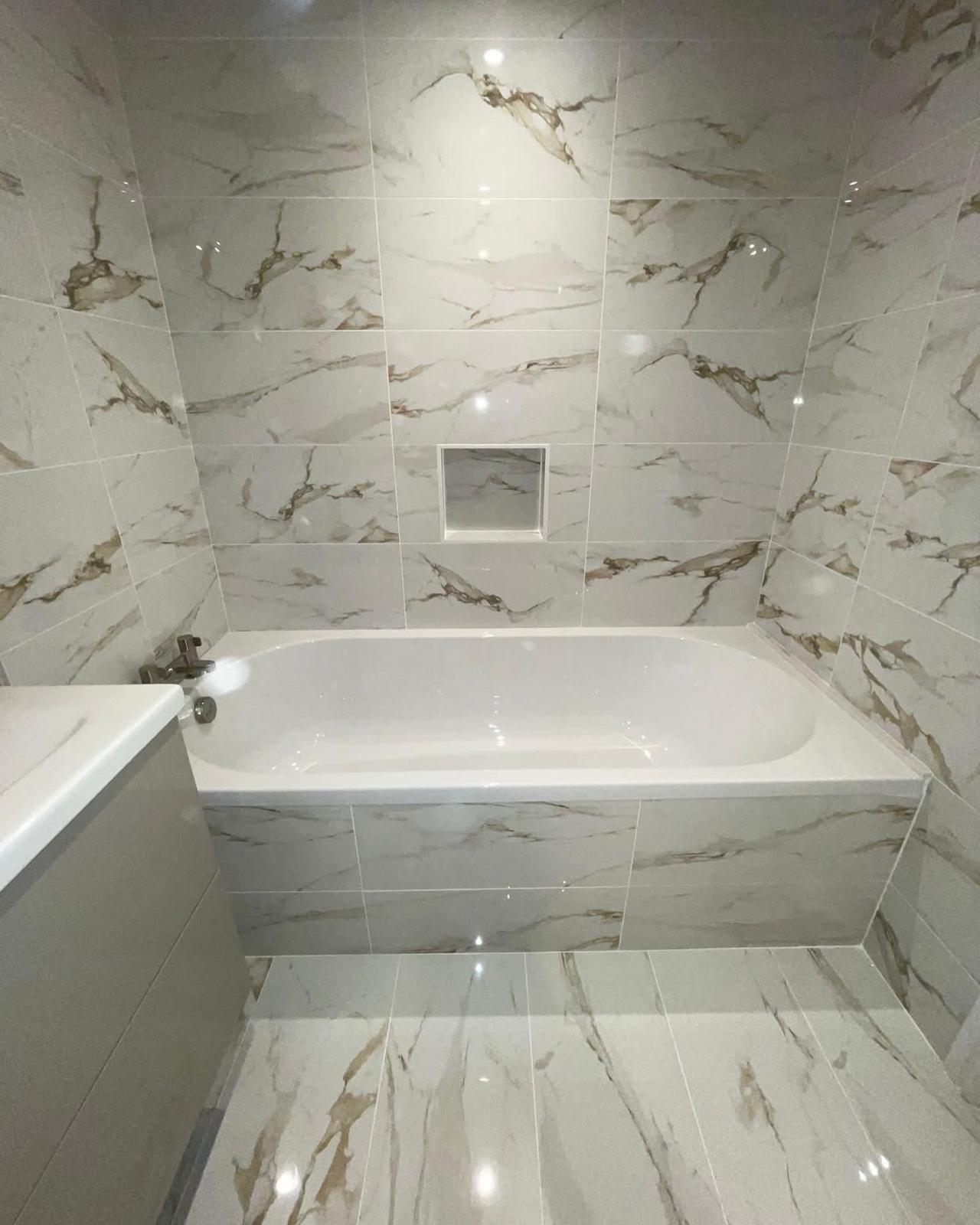 Fully tiled marble effect bathroom with built-in bath and recessed niche