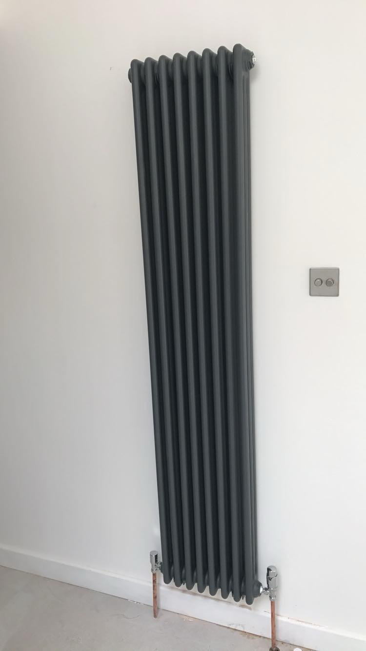 Tall anthracite column radiator installed on a plastered wall with chrome valves