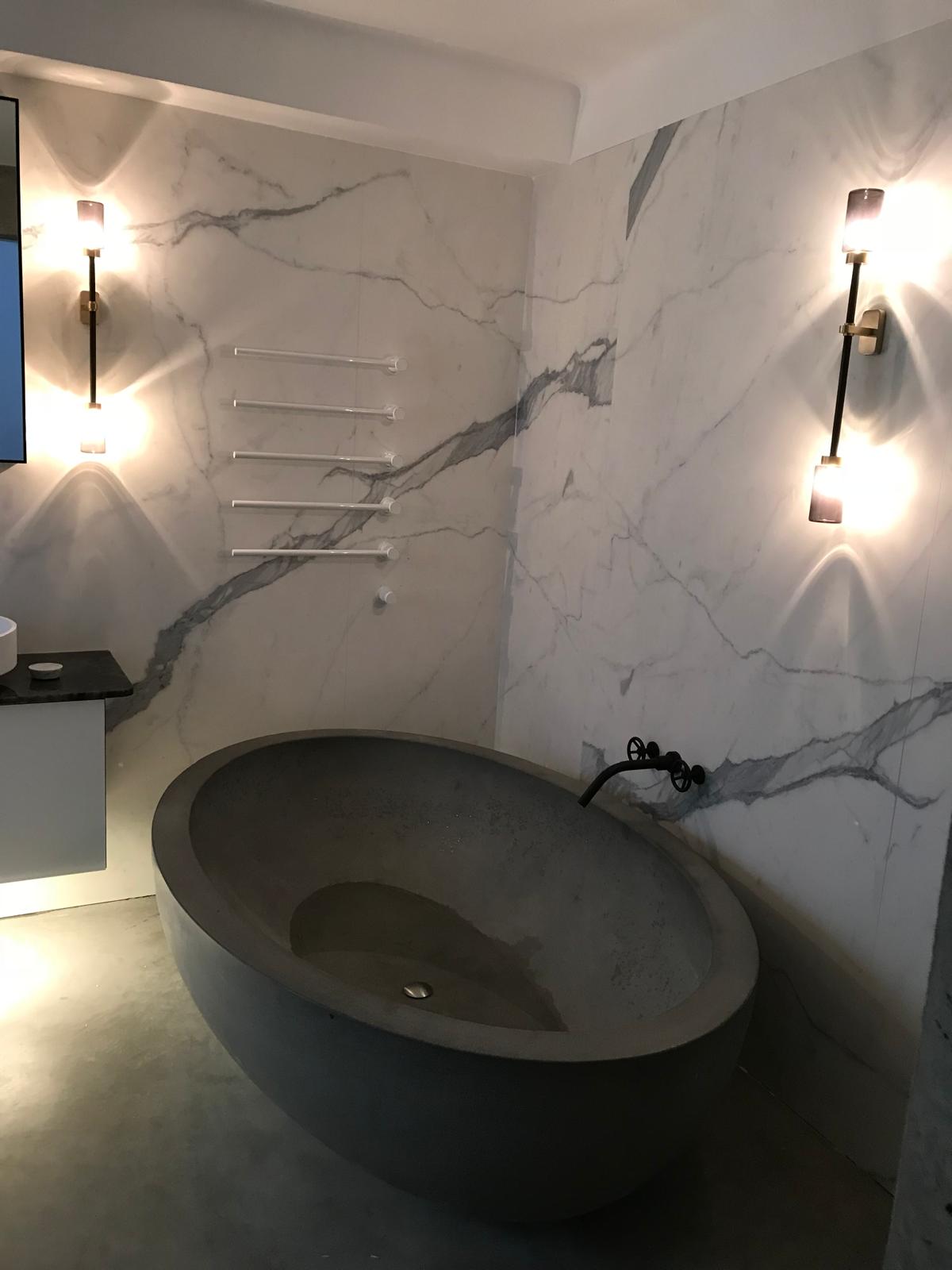 Marble effect bathroom with freestanding stone bath and wall-mounted lighting