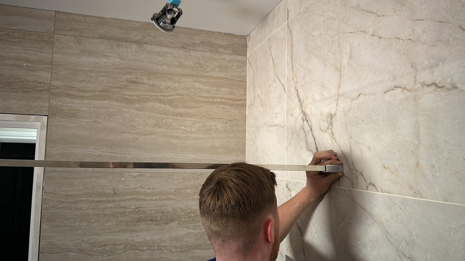 Large-format marble effect tiling being installed on a bathroom wall